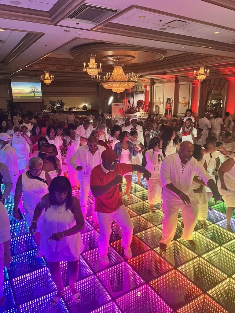 Wedding reception with guests dancing on an LED infinity mirror dance floor and vibrant lighting.
