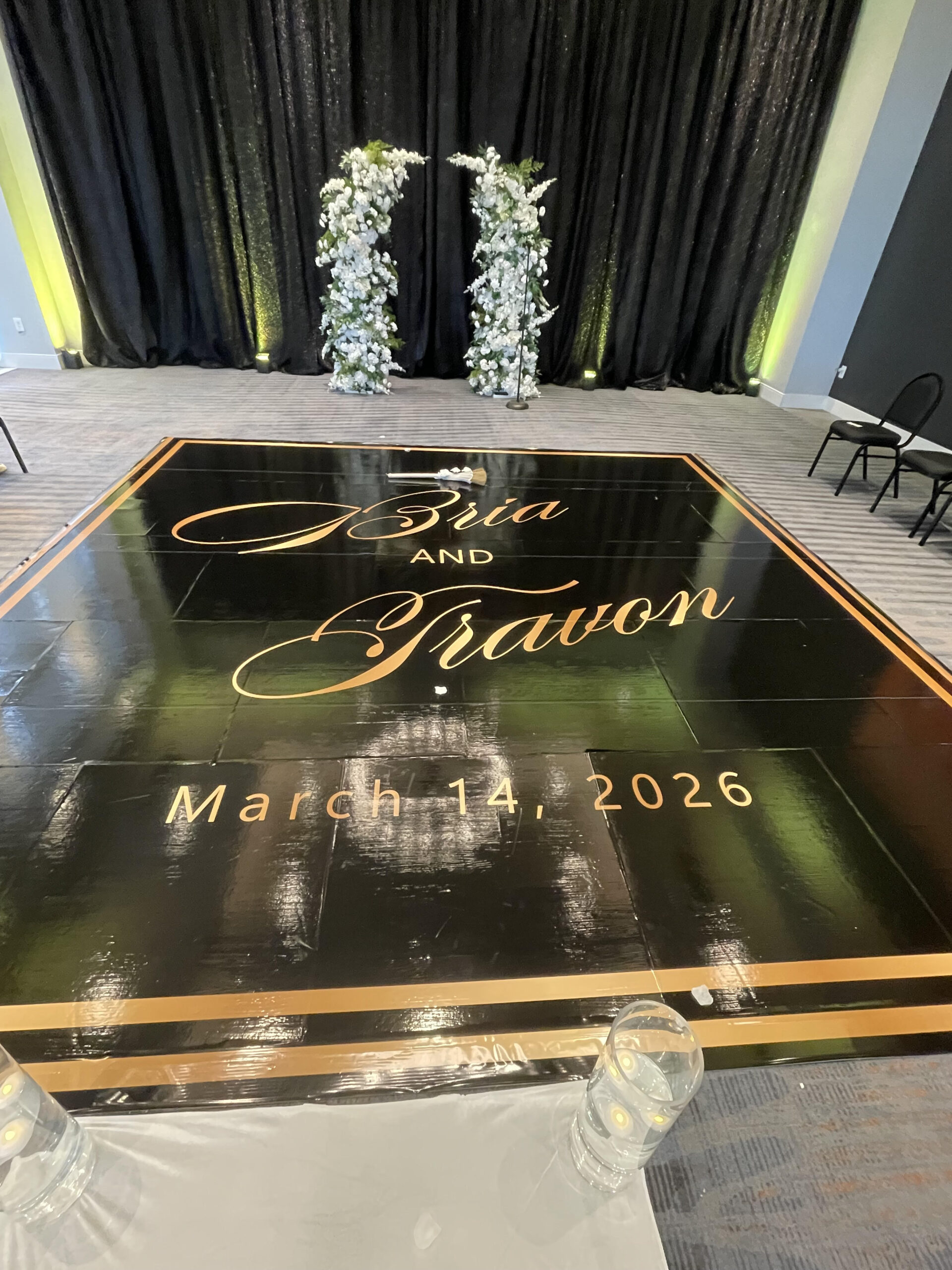 Elegant black and gold wedding reception dance floor with floral arch backdrop.